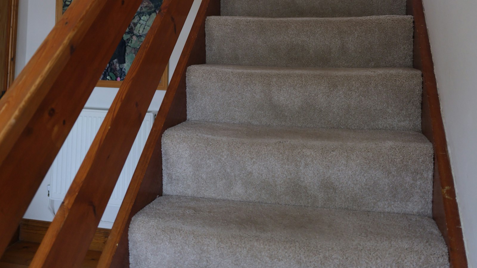 Staircase with beige cut pile carpet and a wood handrail leading up to a window
