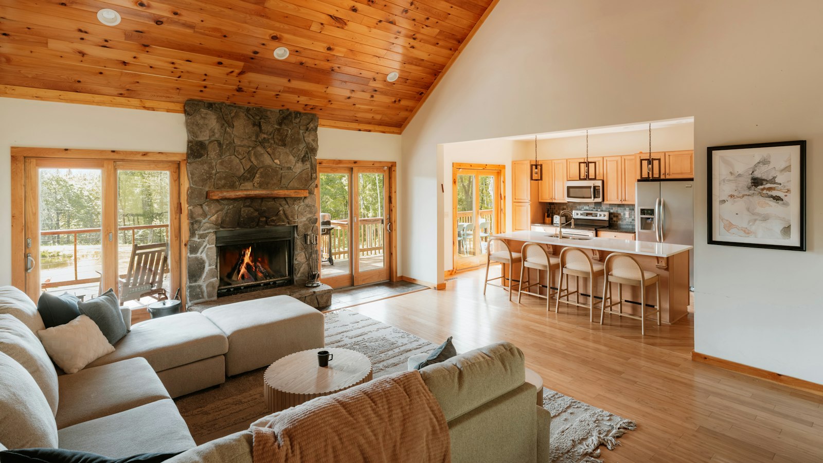 Colorado great room with warm wood flooring, a stone fireplace, sectional sofa and an open kitchen beyond