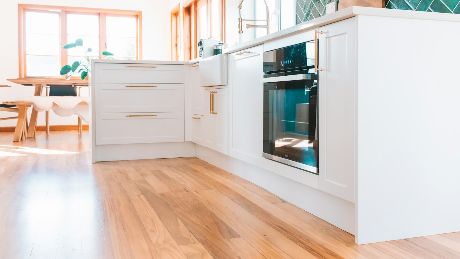 Bright white kitchen with warm wood flooring, a farmhouse sink and a dining table by the windows