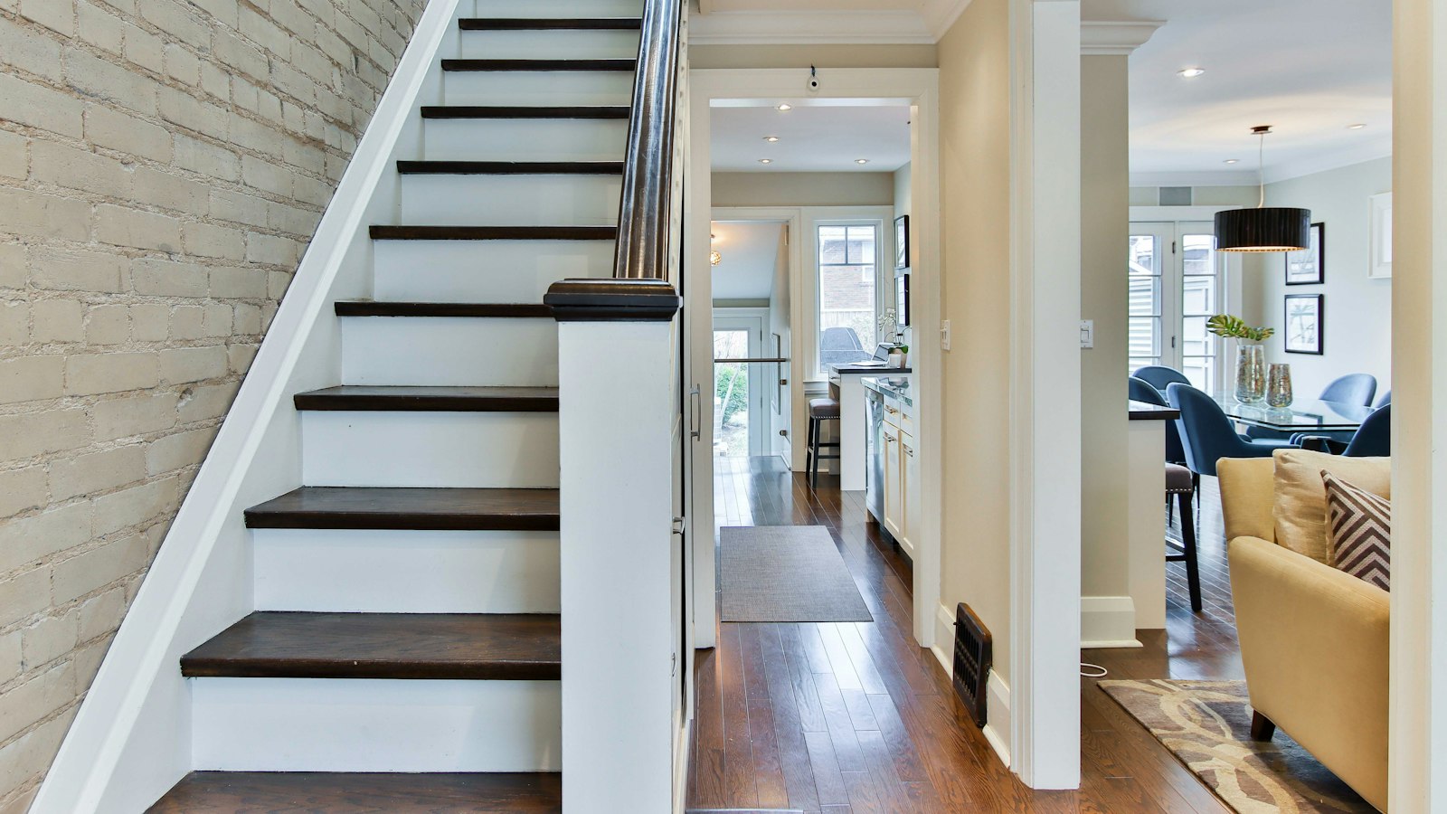 Staircase with dark hardwood treads and white risers beside a white brick wall in an open home