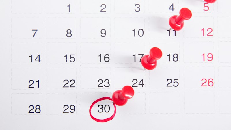 Wall calendar with red push pins marking dates while planning the best time to buy flooring