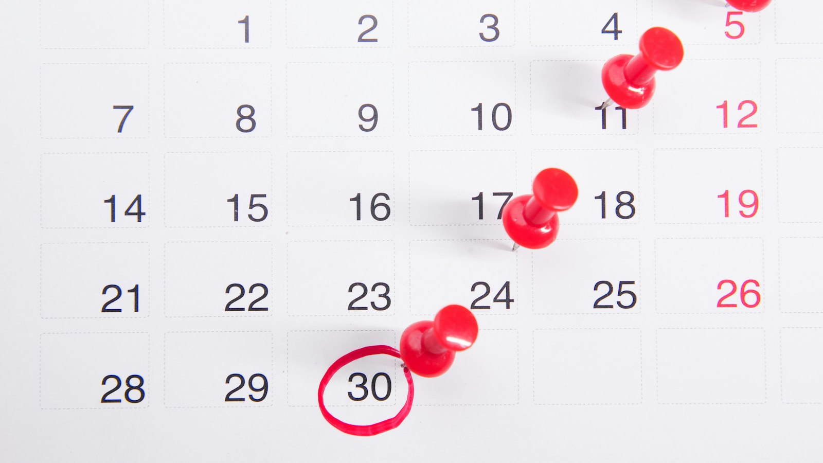 Wall calendar with red push pins marking dates while planning the best time to buy flooring