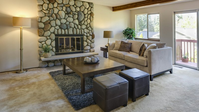 Living room with plush wall-to-wall carpet, a stone fireplace and neutral sofas