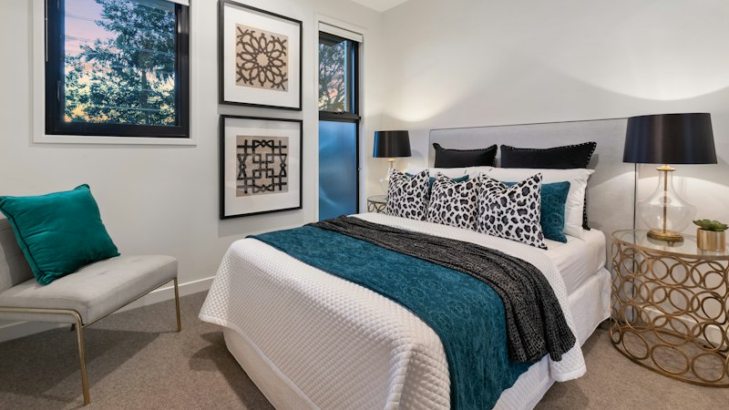Bedroom with new beige wall-to-wall carpet, a made bed and teal accents