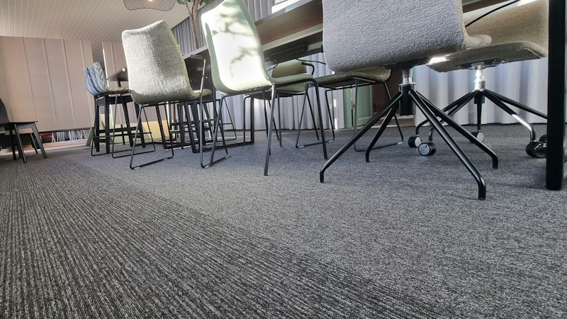 Large room with wall-to-wall gray carpet under rows of chairs and tables