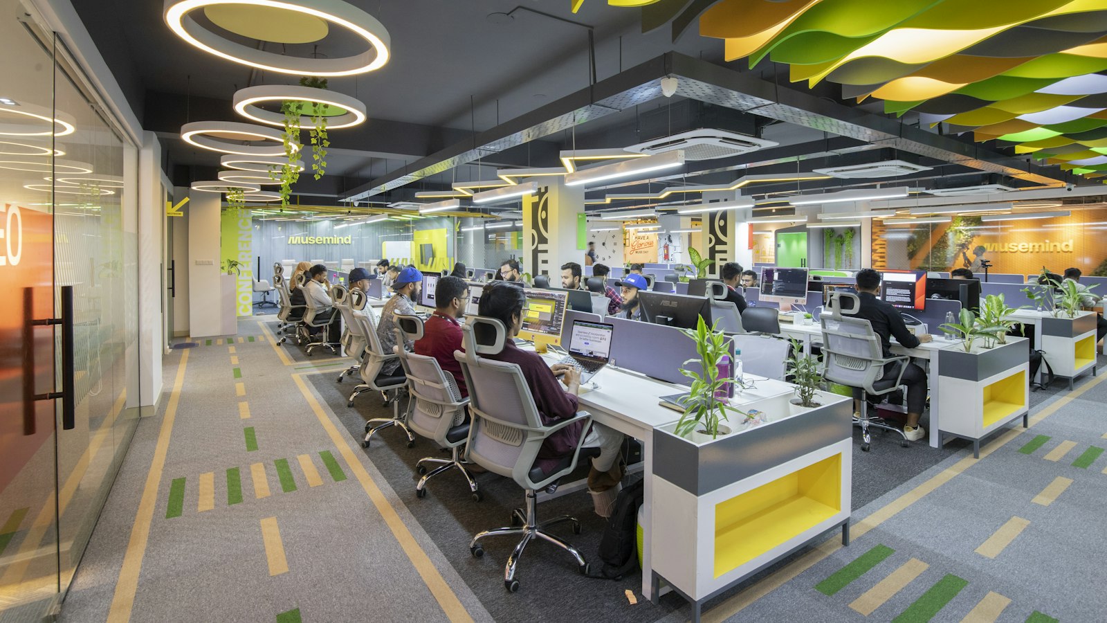 Open-plan office with gray carpet tile and colored wayfinding stripes between rows of desks