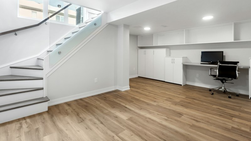 Finished basement with wood-look flooring, a white staircase and a built-in desk