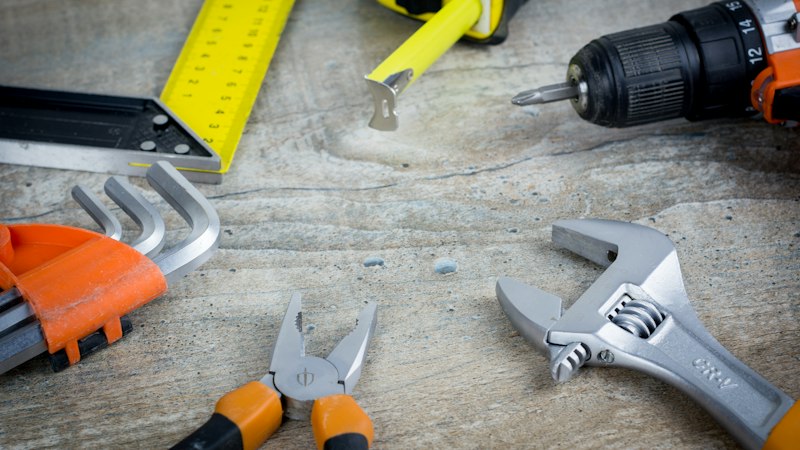Flooring tools including a level, tape measure, drill and wrench on a concrete floor