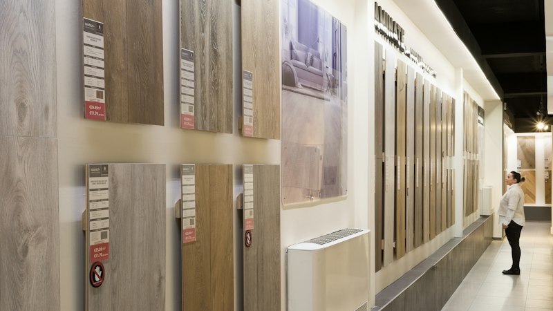 Shopper comparing wood-look flooring samples with price and spec labels on a showroom wall