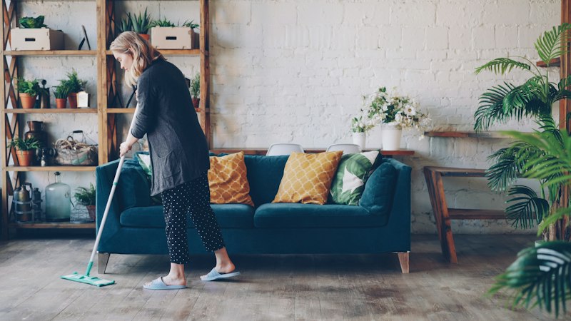 Woman damp-mopping a wood-look floor with a microfiber flat mop in a bright living room