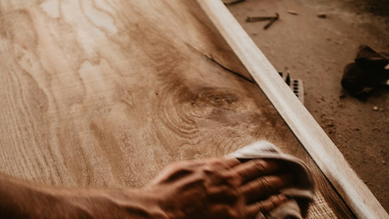 Hand wiping a hardwood plank with a soft cloth during routine hardwood floor care