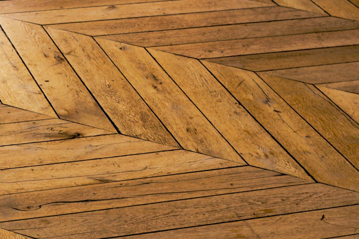 Wood floor boards meeting along a straight center seam in a chevron-style pattern
