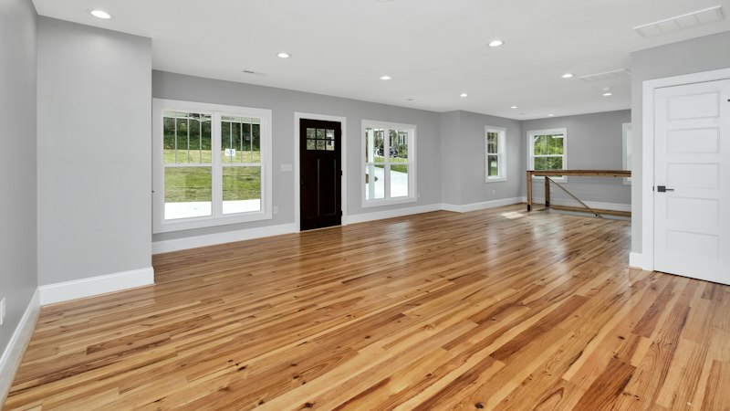 Large empty room with newly installed natural hardwood flooring and white trim