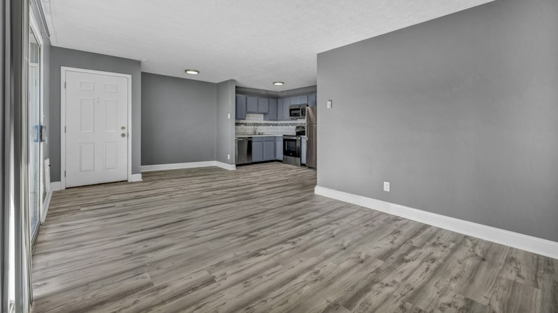 Open living room with gray wood-look plank flooring leading into the kitchen