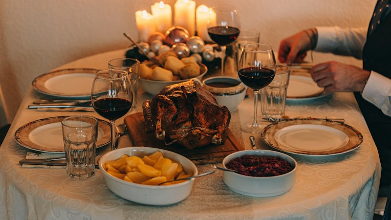 Holiday dinner table with candles, a roast turkey and wine glasses set for guests