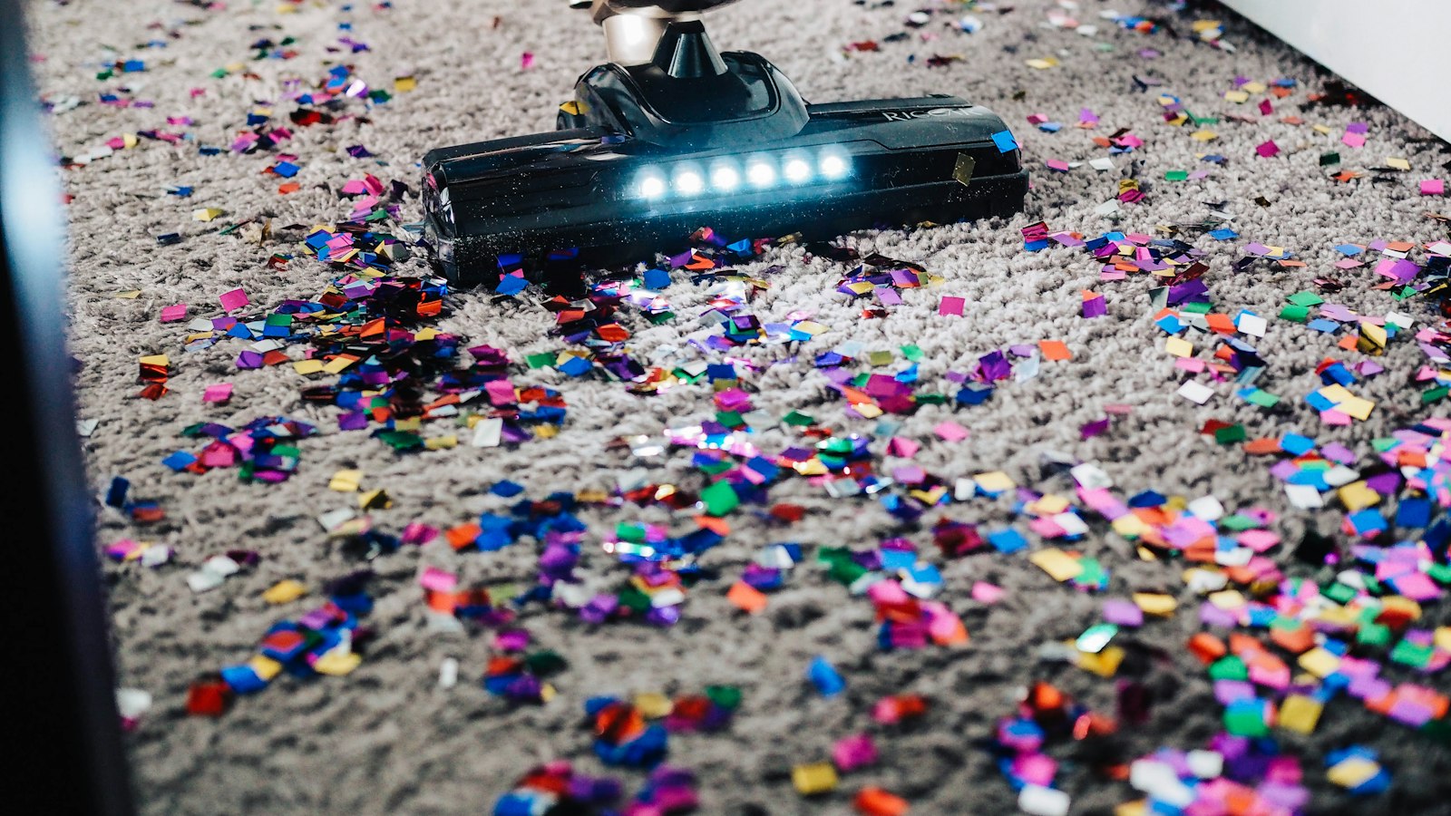 Cordless vacuum cleaning colorful confetti out of a beige carpet
