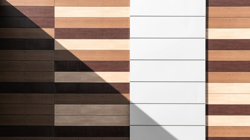 Wood flooring planks in light, medium and dark tones lined up side by side with a band of sunlight across them