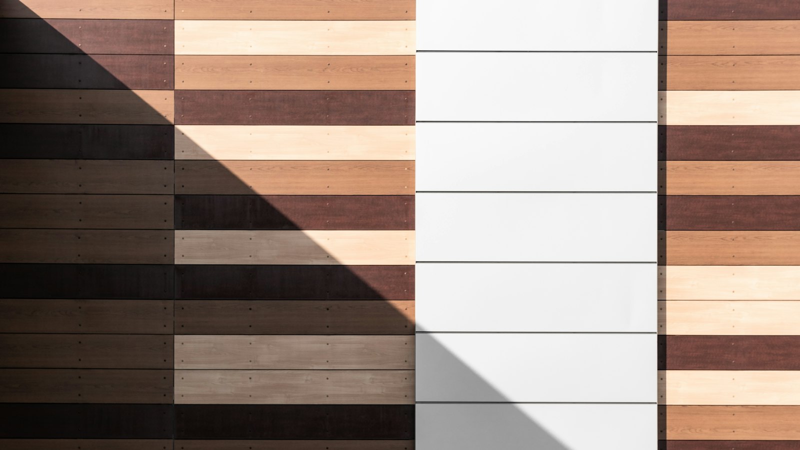 Wood flooring planks in light, medium and dark tones lined up side by side with a band of sunlight across them