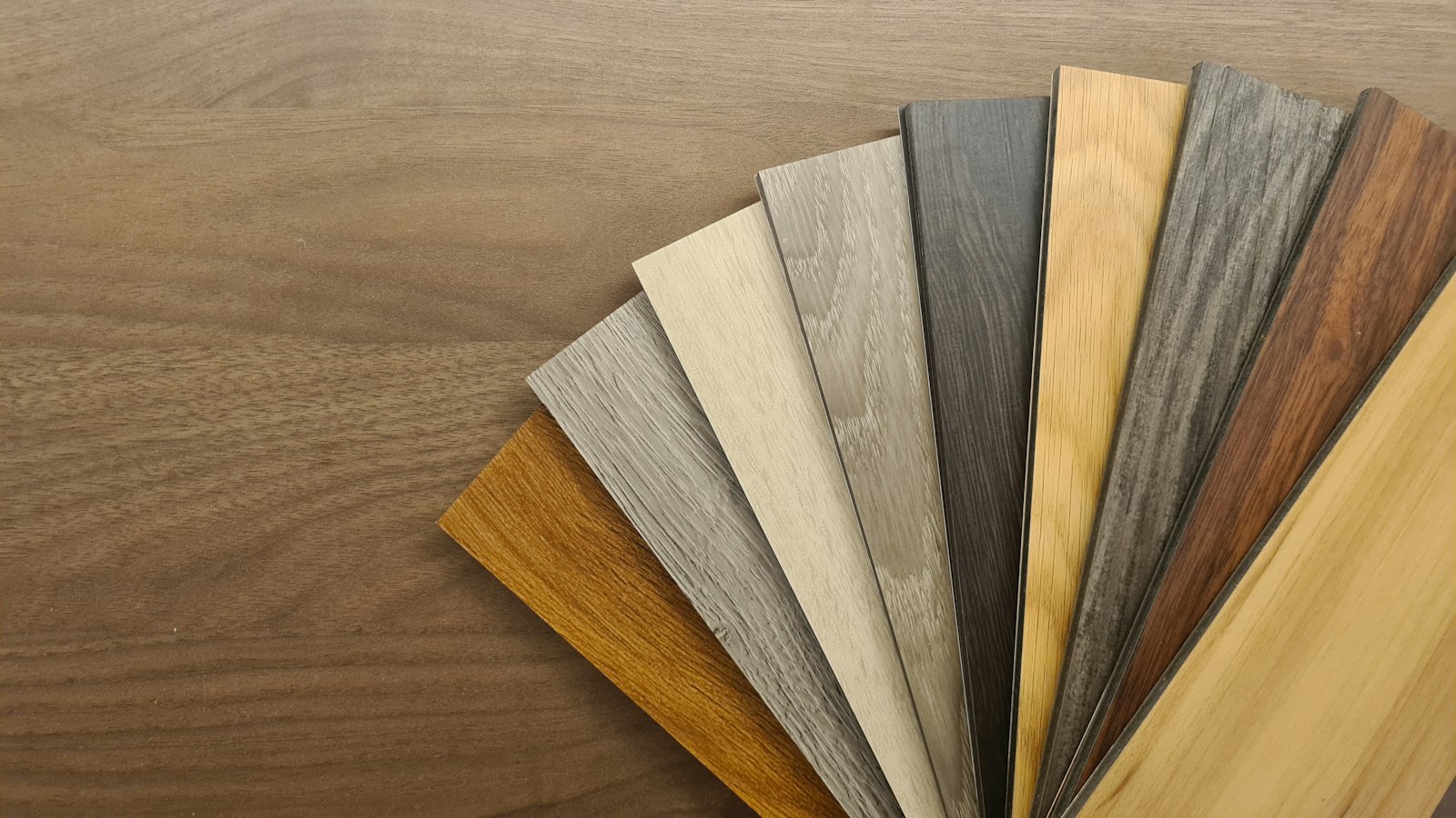 Fan of wood-look luxury vinyl plank samples in oak, gray and walnut tones for comparing options