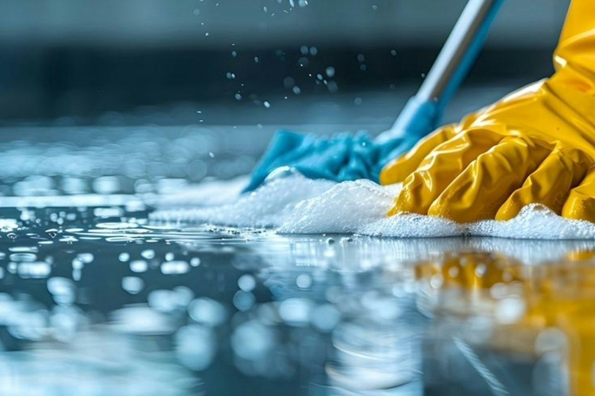 Gloved hand wiping a hard floor with a damp microfiber mop and cleaning solution