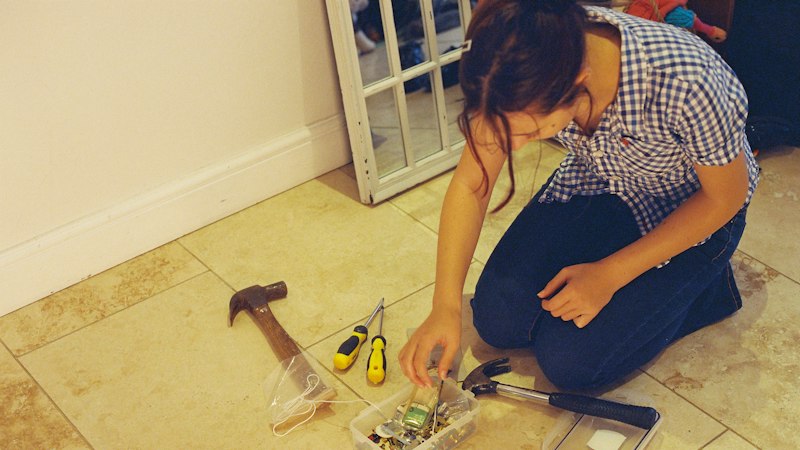 Homeowner kneeling on an existing tile floor sorting tools before a flooring project