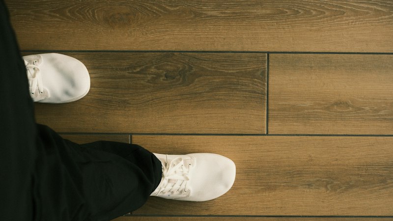 Overhead view of white sneakers on brown wood-look plank flooring with tight seams