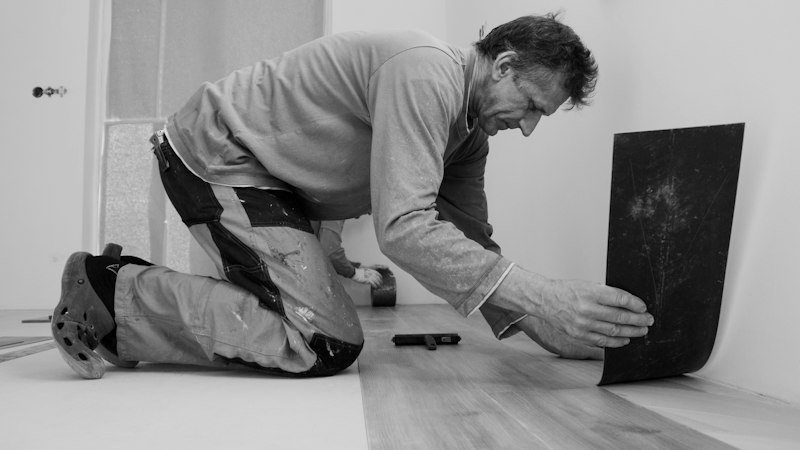 Flooring installer kneeling to fit a new floor piece against the wall