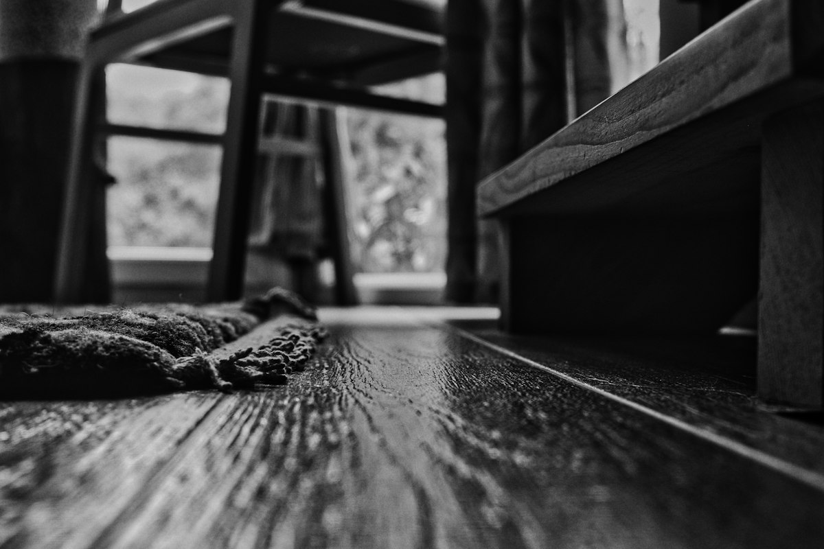 Low-angle black and white close-up of a plank floor surface showing texture and grain