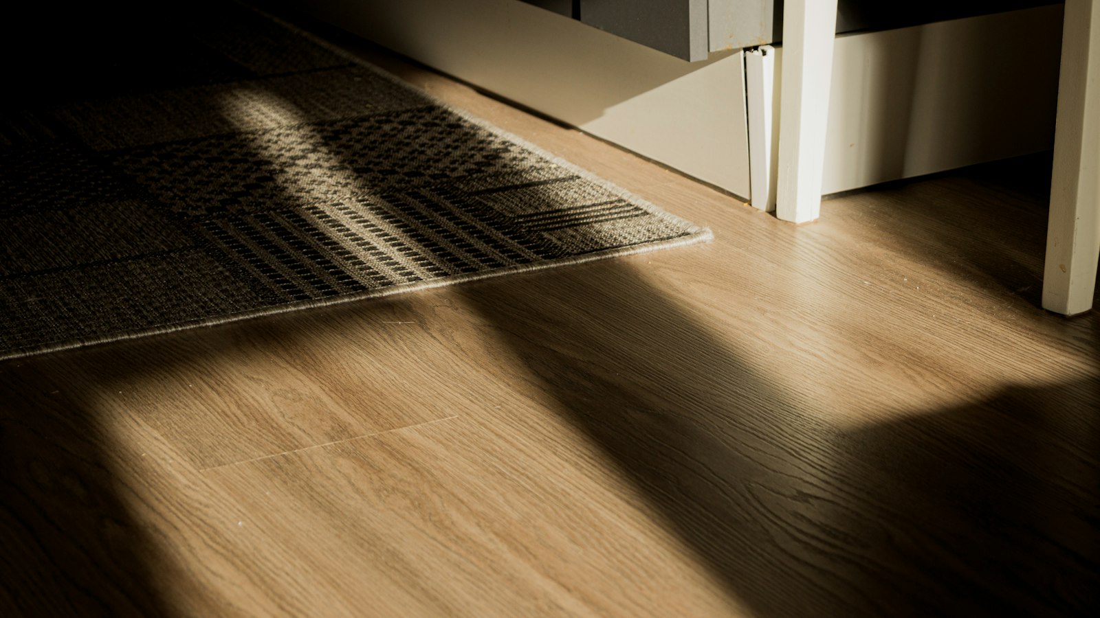 Sunlight across wood-look luxury vinyl plank flooring next to a doormat by the door