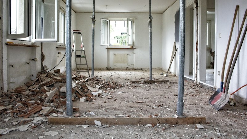 Room mid-renovation with old flooring torn out, debris piled up and temporary support posts