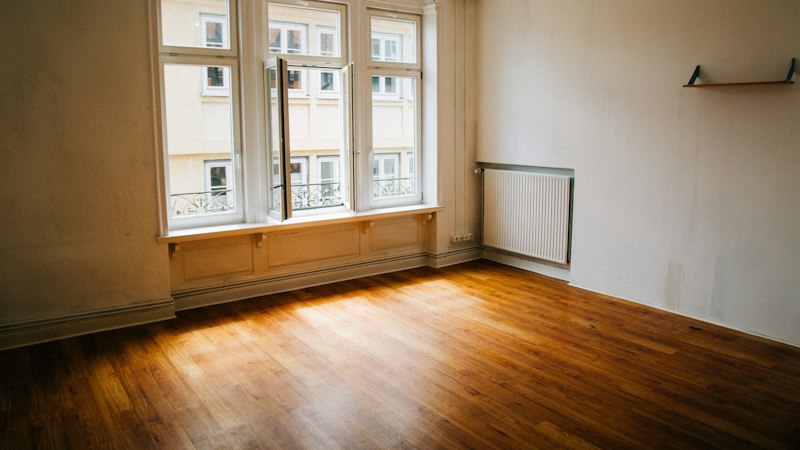 Empty room with freshly refinished glossy hardwood floors catching window light