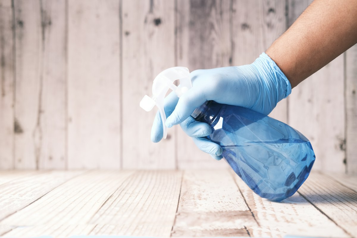 Gloved hand holding a blue spray bottle of cleaner ready to treat a floor stain