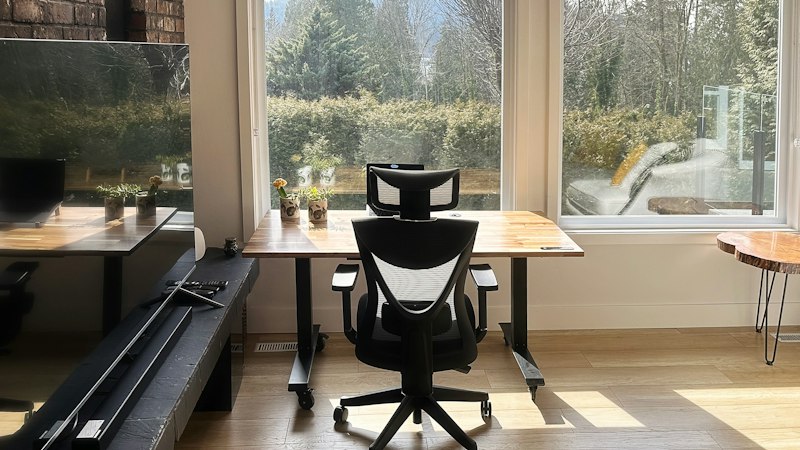 Home office with light wood flooring, an ergonomic chair and large windows