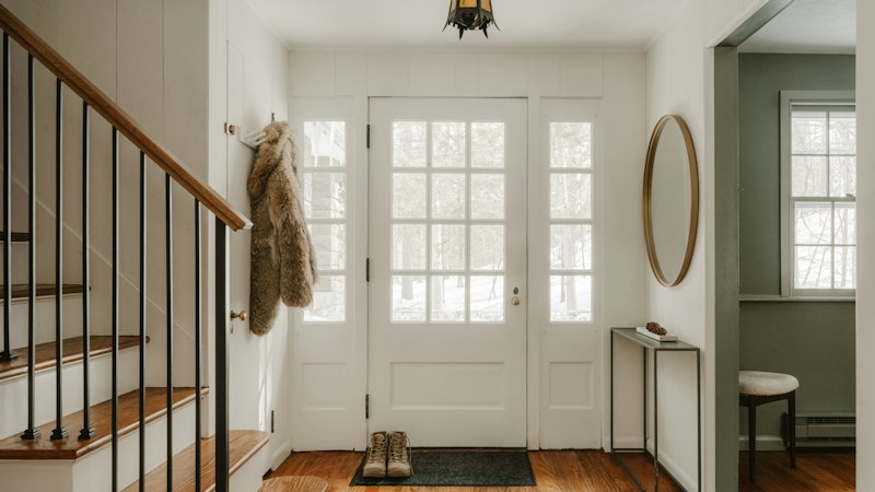 Front entryway with boots on a door mat, wood flooring and a staircase, ready for muddy season
