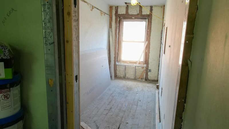 Room under renovation with a bare subfloor, open wall framing and a window